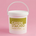 White bucket of 'Green Stachio' pistachio spread on a pink background