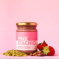 Jar of Pink Stachio spread with pistachios and strawberries on a pink background
