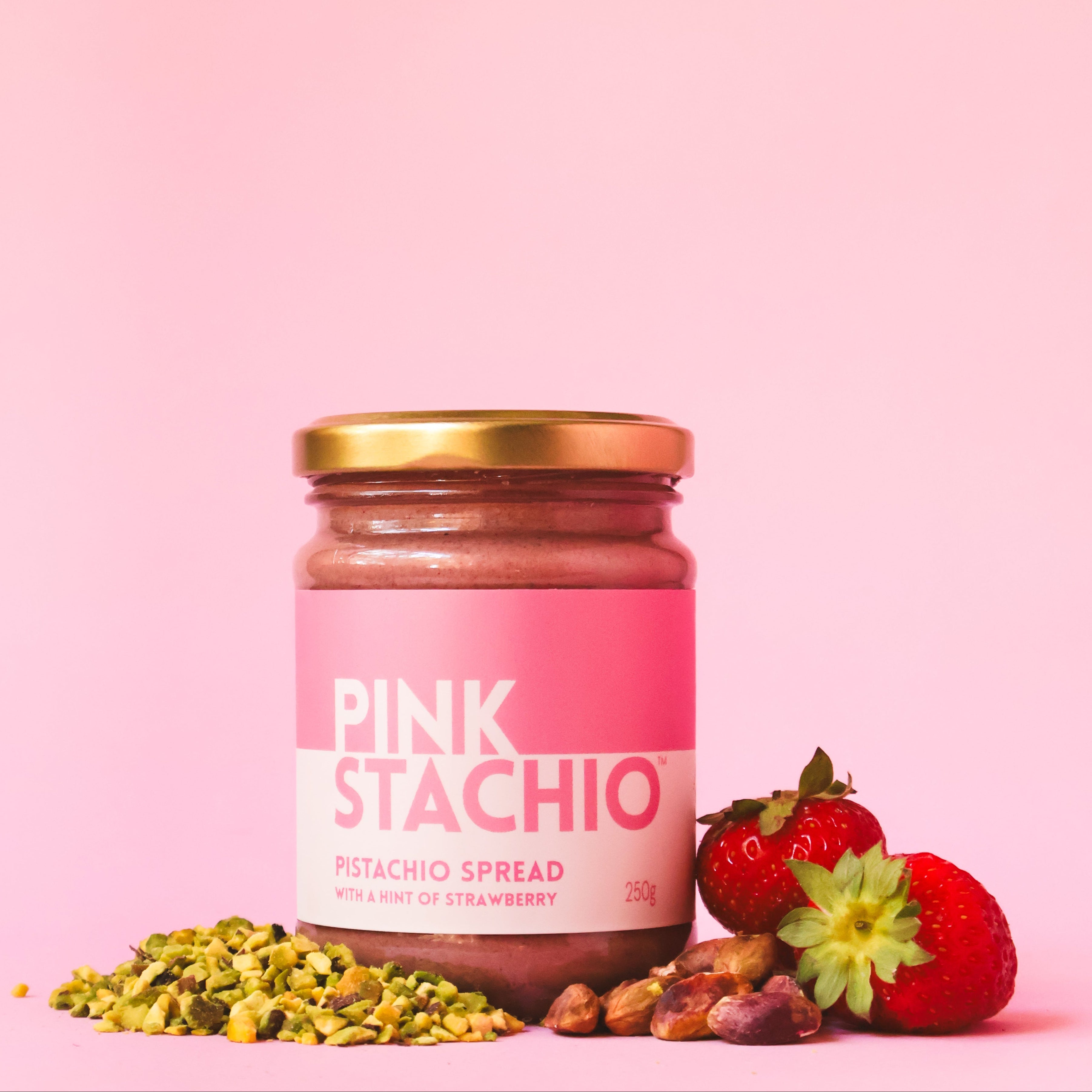 Jar of Pink Stachio spread with pistachios and strawberries on a pink background